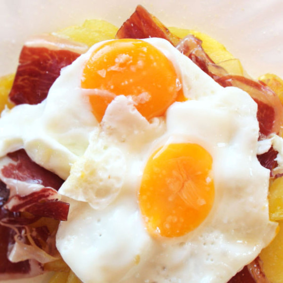 A serving og huevos estrellados with potatoes, ham, and eggs on top
