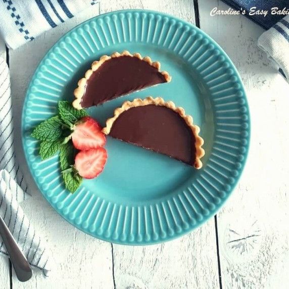 Overhead image on white wooden table of blue plate with 2 halves of a chocolate tart with berries.