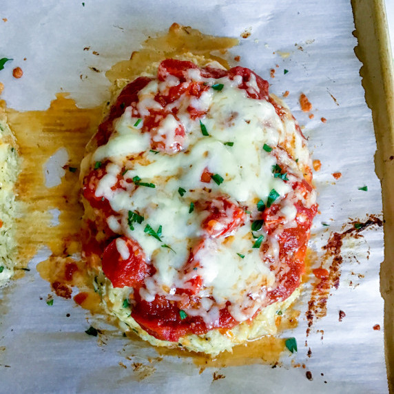 Ground turkey meatloaf topped with roasted fresh tomatoes and mozzarella cheese on top of parchment.