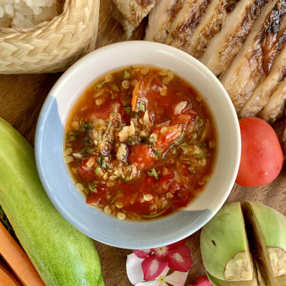 Top-view of jeow som dipping sauce with grilled meat, fresh vegetables, and sticky rice.