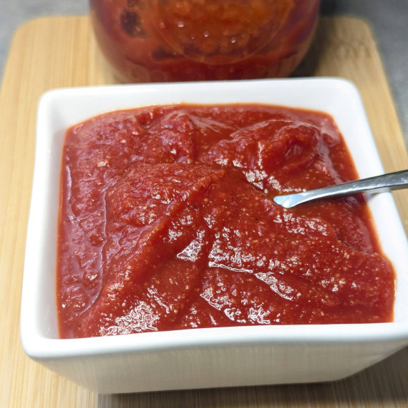A square white bowl filled with homemade ketchup.