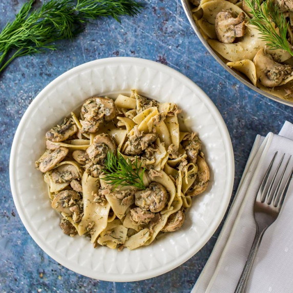 Overhead shot of lemon dill tuna and noodles garnished with herbs in a white bowl on a blue placemat