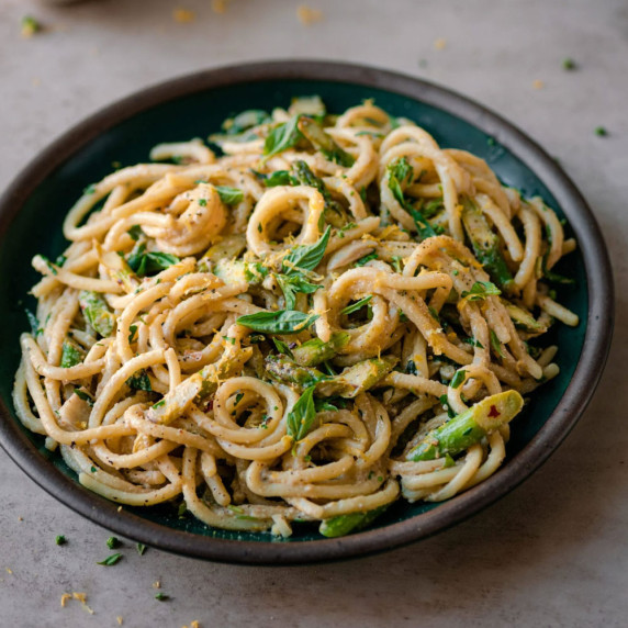 45 degree angle of lemon asparagus pasta in a green bowl on a brown countertop. 