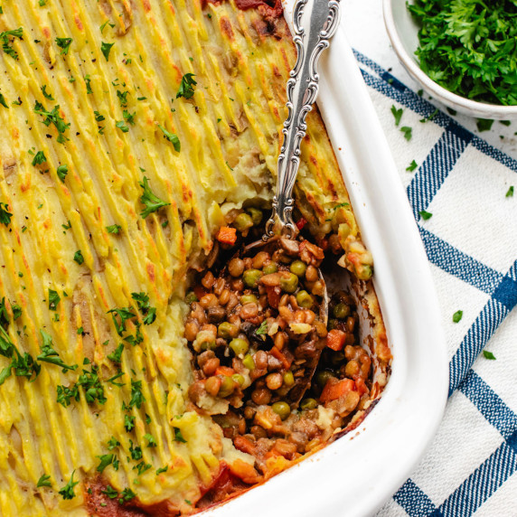 Vegan shepherd's pie in a white baking dish with a serving spoon.
