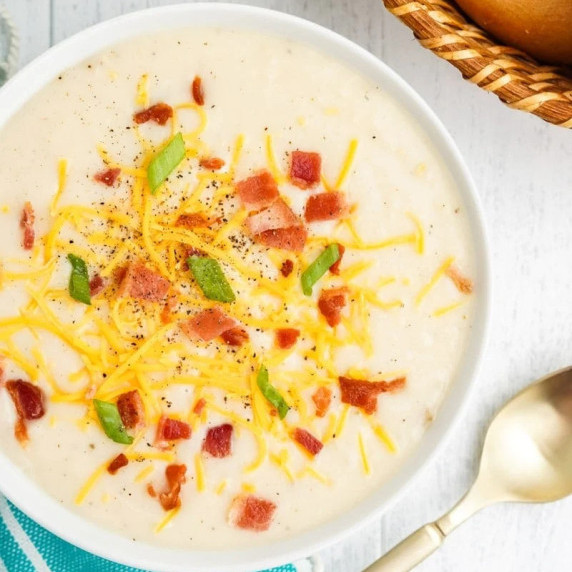 Top view of a bowl of mashed potato soup topped with shredded cheese, bacon bits, and green onions.