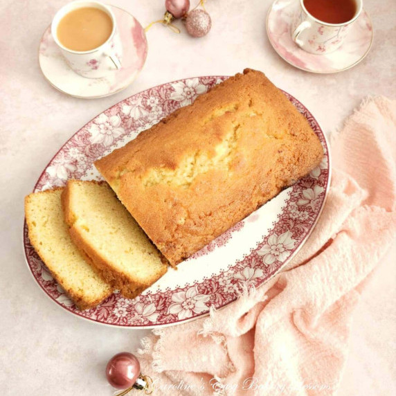 Overhead image of pink table with napkin & crockery around a Madeira loaf cake.