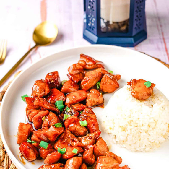 Sticky bourbon chicken garnished with green onions on a plate.