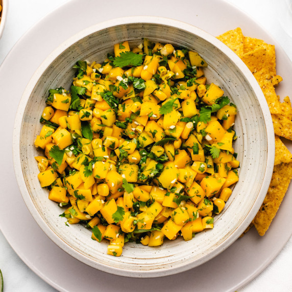 Mango corn salsa with cilantro in a bowl with tortilla chips on the side.
