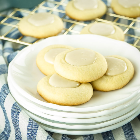 Side close up shot of four maple thumbprint cookies on a stack of white plates with more in the back
