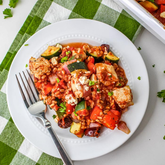 Overhead shot of a fork picking up a piece of chicken from a plate of casserole with feta. 