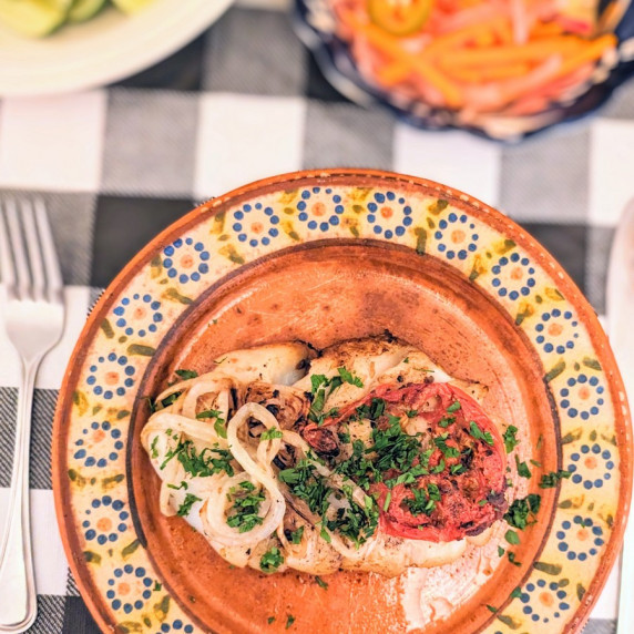 Middle Eastern grilled cod topped with tomato, onion, and tamarind on a clay plate