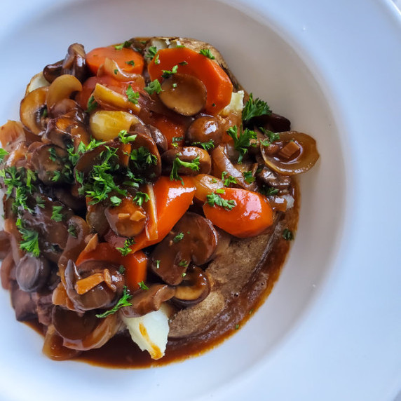 Baked potato stuffed with bourguignon on a white plate with a marble background.