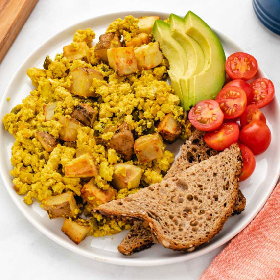 Hatch green chile tofu scramble with potatoes on a plate with toast, tomatoes, and avocado slices.