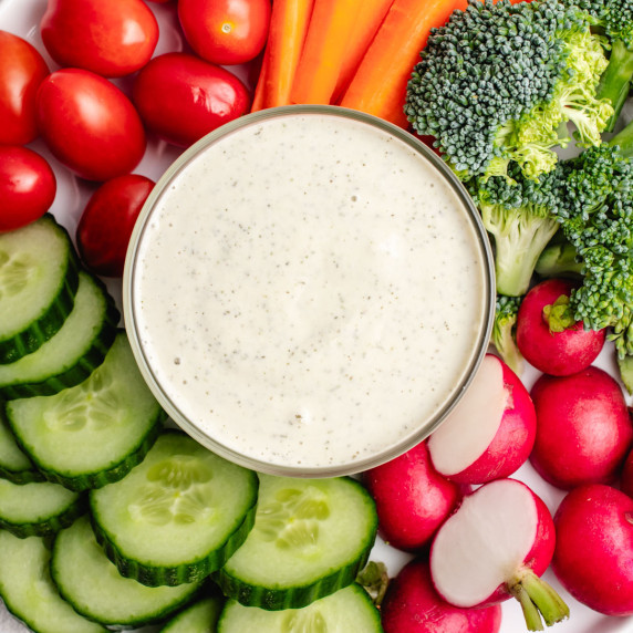 Vegan ranch dressing in a bowl with cucumbers, radishes, cherry tomatoes, broccoli, and carrots.