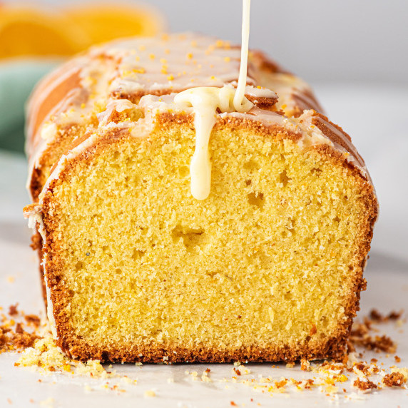 sliced orange cardamon loaf cake with orange glaze being poured over