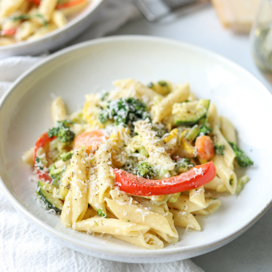 penne primavera in a white stoneware bowl topped with black pepper and parmesan cheese