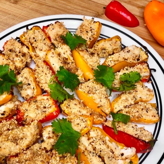 A white plate with roasted red, orange and yellow mini sweet bell peppers filled vegan cheese.