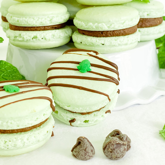 mint chocolate macarons with a chocolate drizzle on a pedestal on a white tablecloth