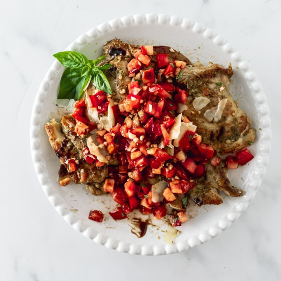 chicken on a white plate topped with diced tomatoes.