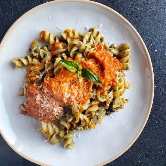 Pesto coated rotini pasta finished with pepper sauce on a white plate with a black background.