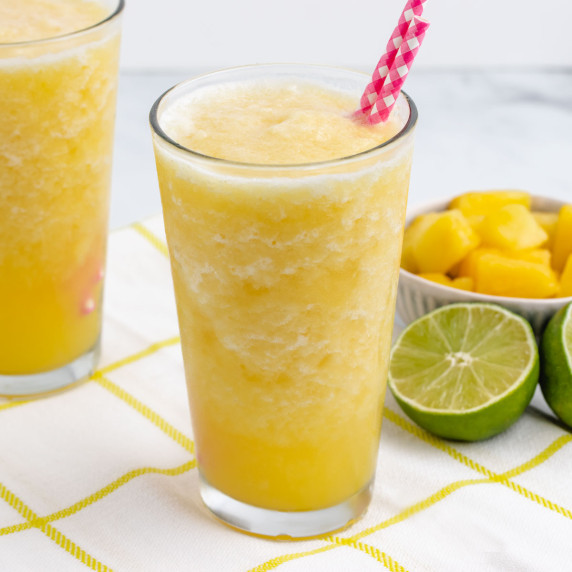 Pineapple slushie with pink straws in a glass with limes in the background.