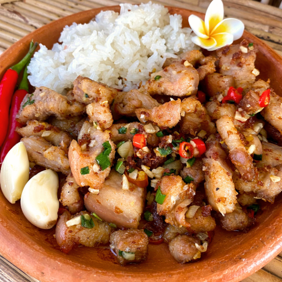 Pork belly chili garlic in a clay dish with red chilies, 2 cloves of garlic, and white rice.