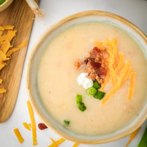 Overhead shot of potato soup garnished with shredded cheese, bacon, chives, and sour cream.