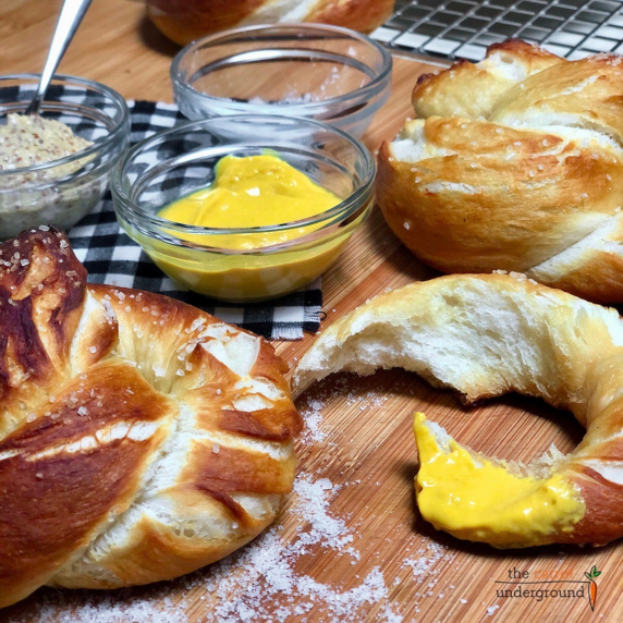 Homemade vegan soft pretzels sprinkled with coarse salt and dipped in yellow mustard.