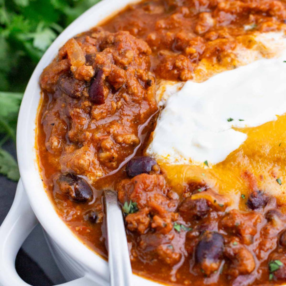 Pumpkin Chili RECIPE scooped inside a white bowl with a metal spoon.