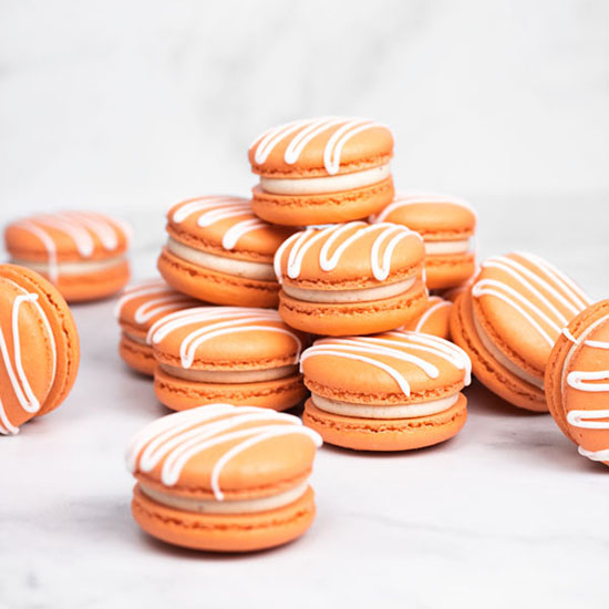 Orange and white pumpkin spice macarons on white countertop