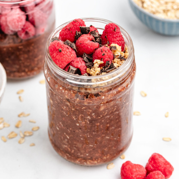 Chocolate raspberry overnight oats in a glass jar with raspberries and chocolate on top.