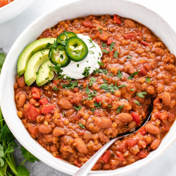 Vegan red lentil chili in a white bowl with avocado and jalapeno slices.