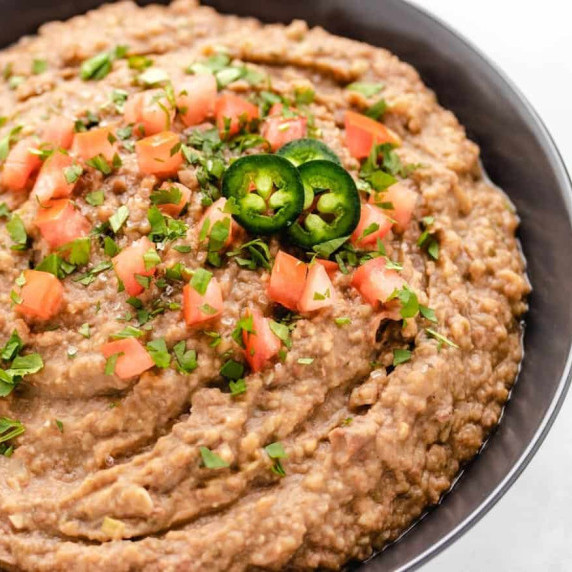 Refried beans in a black bowl with diced tomatoes and jalapeños.