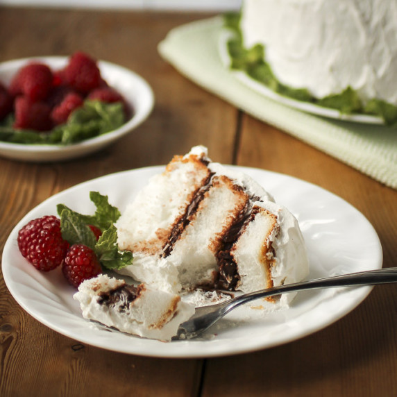 Side shot of a slice of angel food cake in a white bowl with raspberries, mint, and a fork.