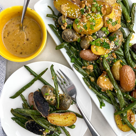 White plate and white platter with roasted potatoes and green beans and maple tahini dressing. 
