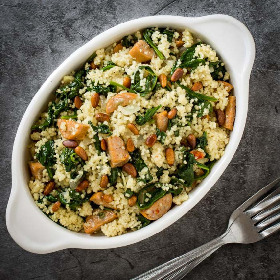Overhead shot of couscous in a white oval dish on a black surface with two metal forks on the side.