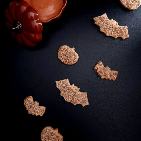 Black background with line of bat & pumpkin shaped sesame topped savoury cookies.