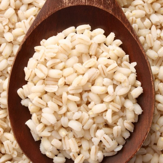 Cooked barley grains in a wooden spoon rest on top of a pile of cooked barley.