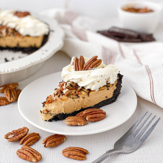Slice of Turtle Pie on a white plate with pecans scattered nearby.