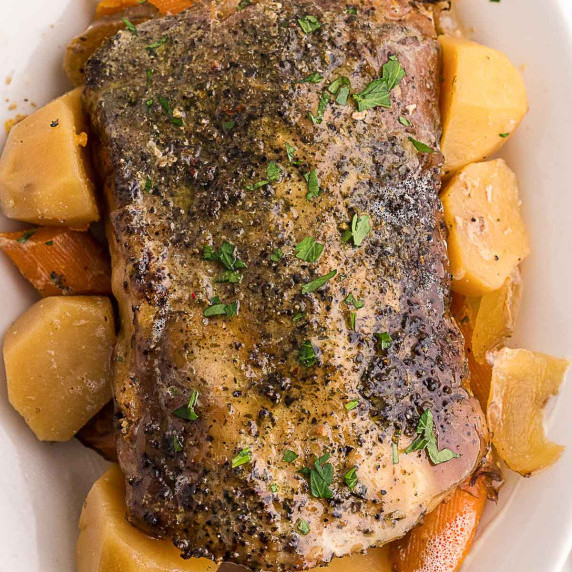 slow cooked pork roast with veggies in a white serving dish