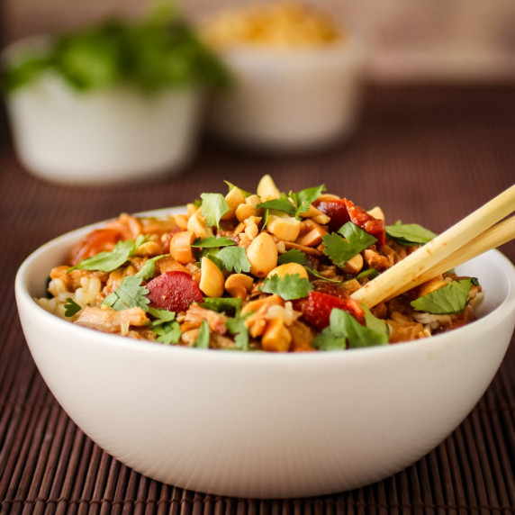 Side view of Thai peanut chicken garnished with herbs in a white bowl on a wooden placemat.