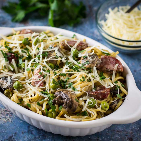 Side shot of turkey tetrazzini garnished with cheese and herbs in a white oval bowl on a speckled bl