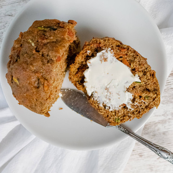 Muffin cut in half on a white plate on a white background with butter smeared on it
