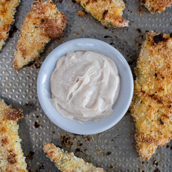 Small white bowl of sweet mayo dip surrounded by baked chicken tenders