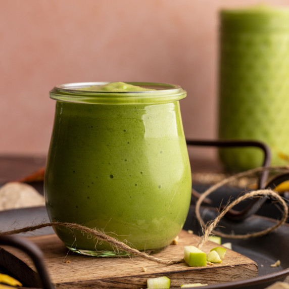 Sour apple smoothie in small jar on wooden coaster.