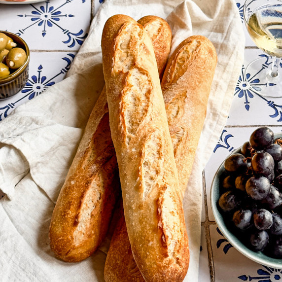 Three freshly baked sourdough baguettes on a white linen tea towel.