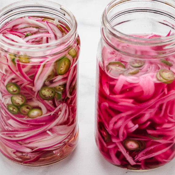 Spicy pickled red onions in a glass jar with sliced serranos.
