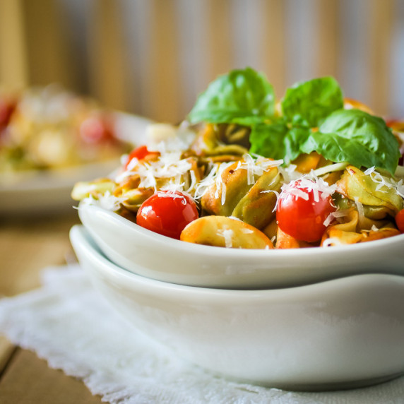 Side shot of tortellini garnished with basil and parmesan cheese in a white bowl.