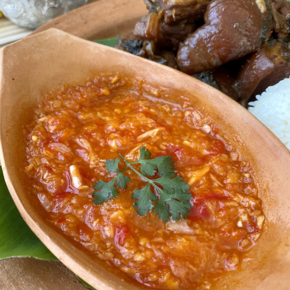 A red spicy vinegar dipping sauce in a clay sauce cup.