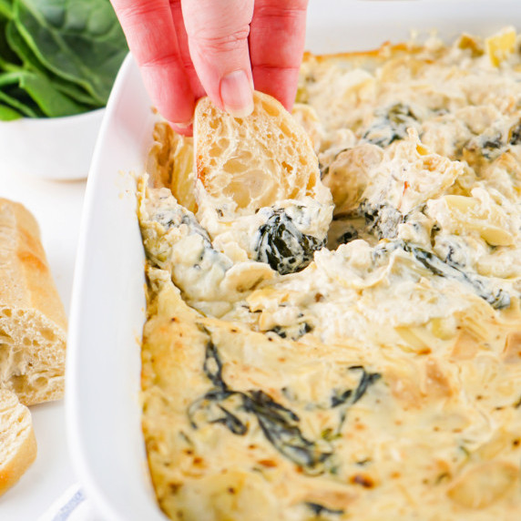 Woman scooping spinach artichoke dip onto a slice of French bread.
